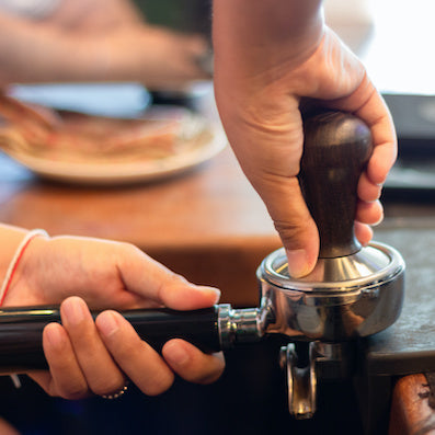 A barista tamps coffee using a tool called a tamper. It compresses the ground coffee into a puck inside the portafilter.